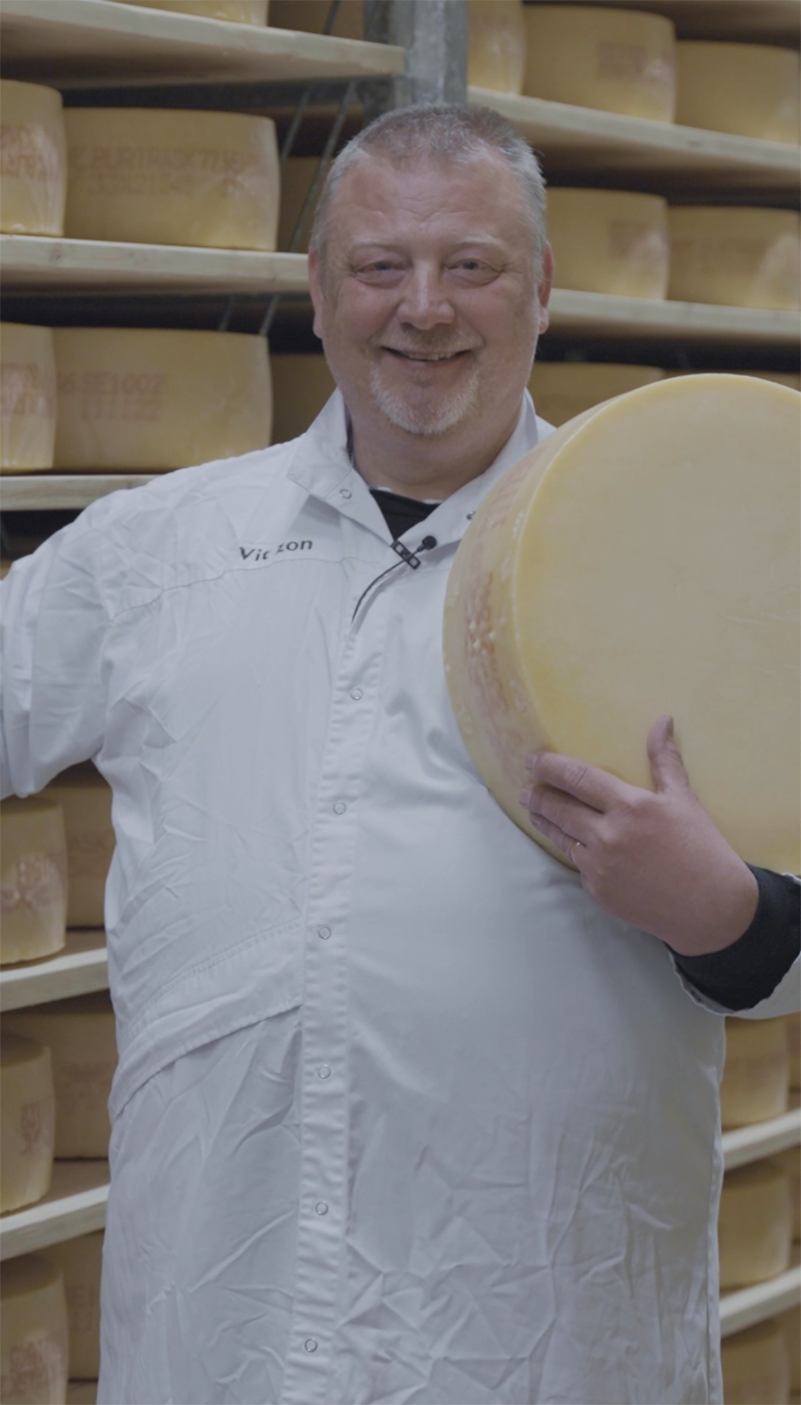 The cheese master between shelves filled with cheese.