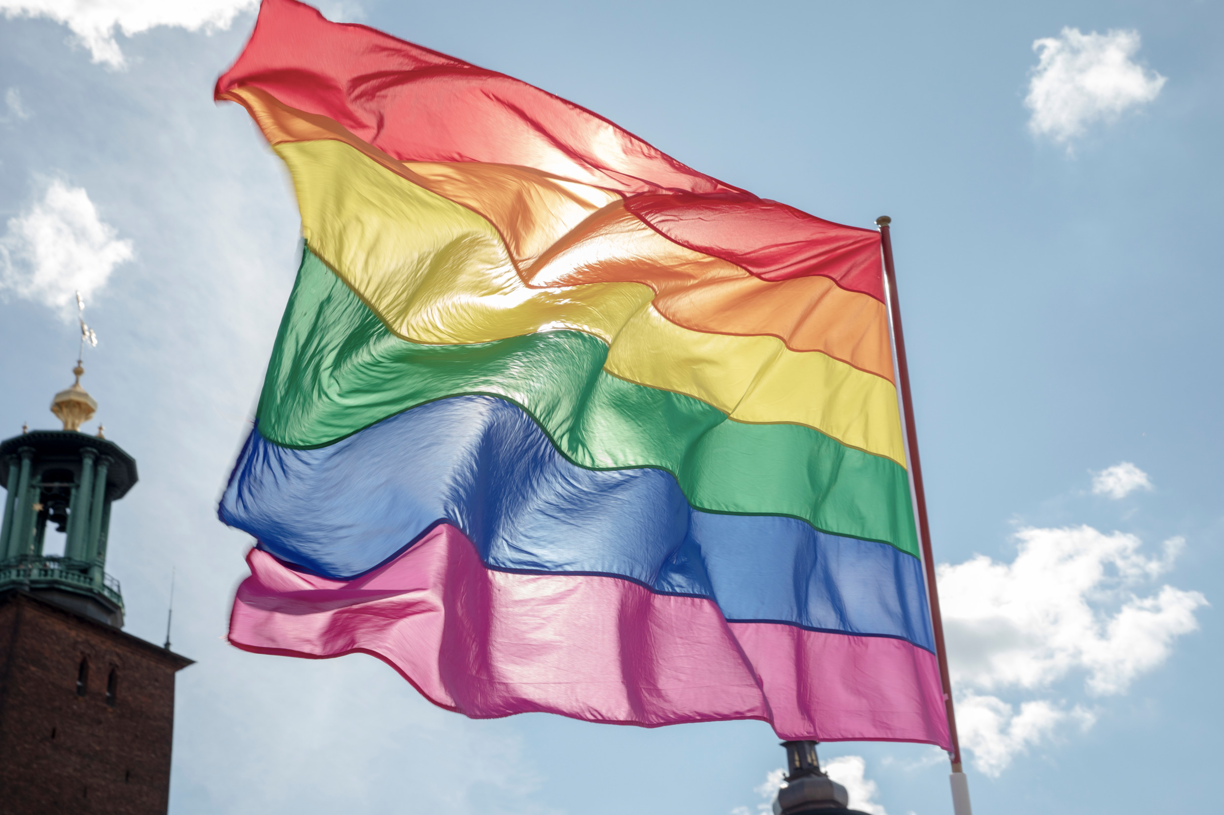 A rainbow flag flutters in the wind. The tower of Stockholm city hall in the background.