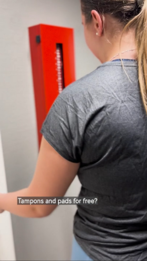 A girl taking free tampons from a red locker.