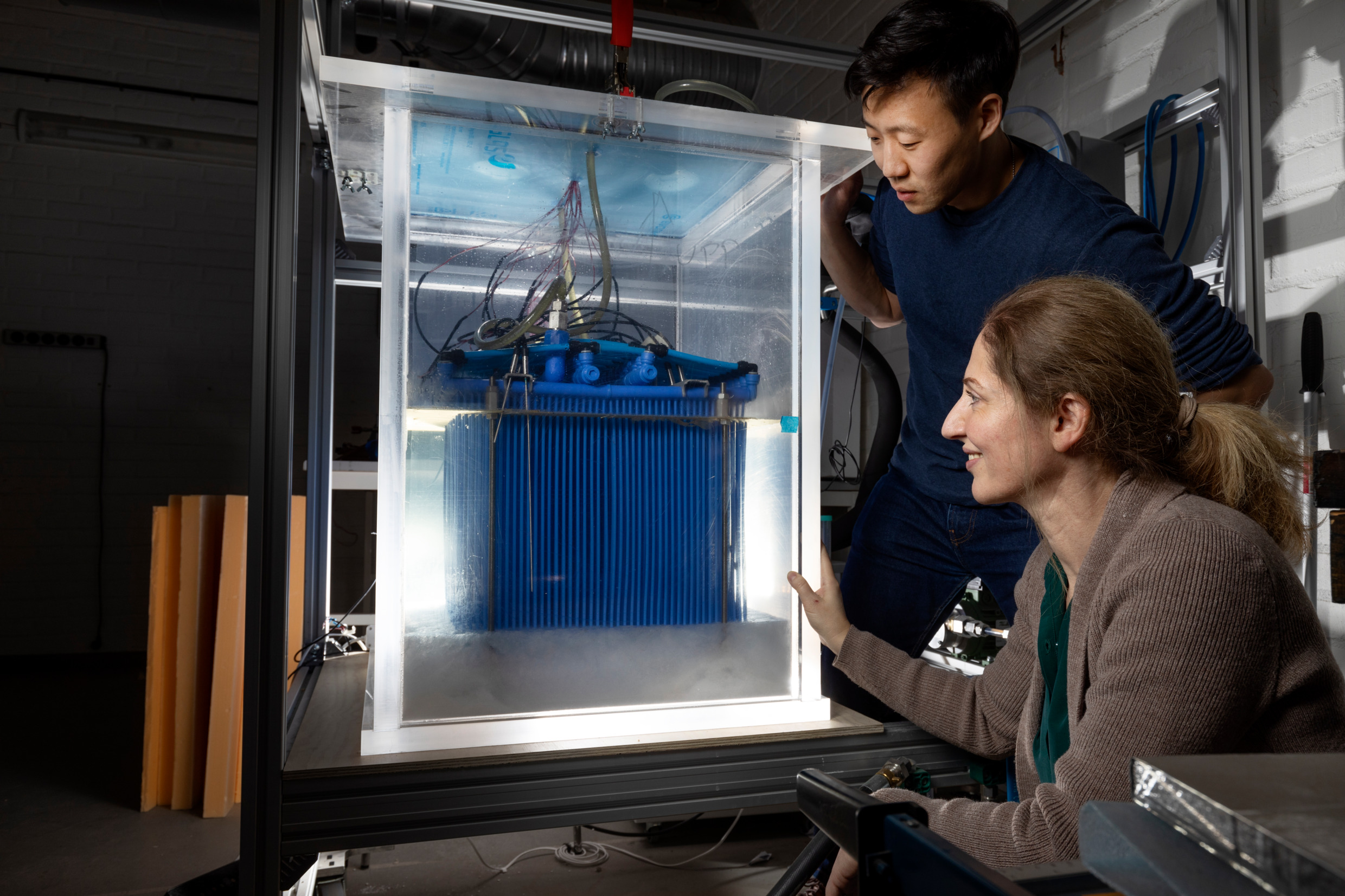 A man and a woman look inside a glass case filled with wires and blue metal container.